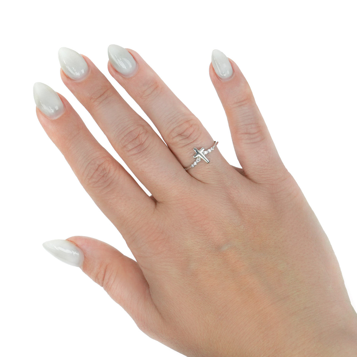 A silver ring with a small cross design worn on the ring finger of a hand with long, manicured white nails, set against a plain white background. [lifestyle]