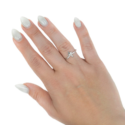 A silver ring with a small cross design worn on the ring finger of a hand with long, manicured white nails, set against a plain white background. [lifestyle]