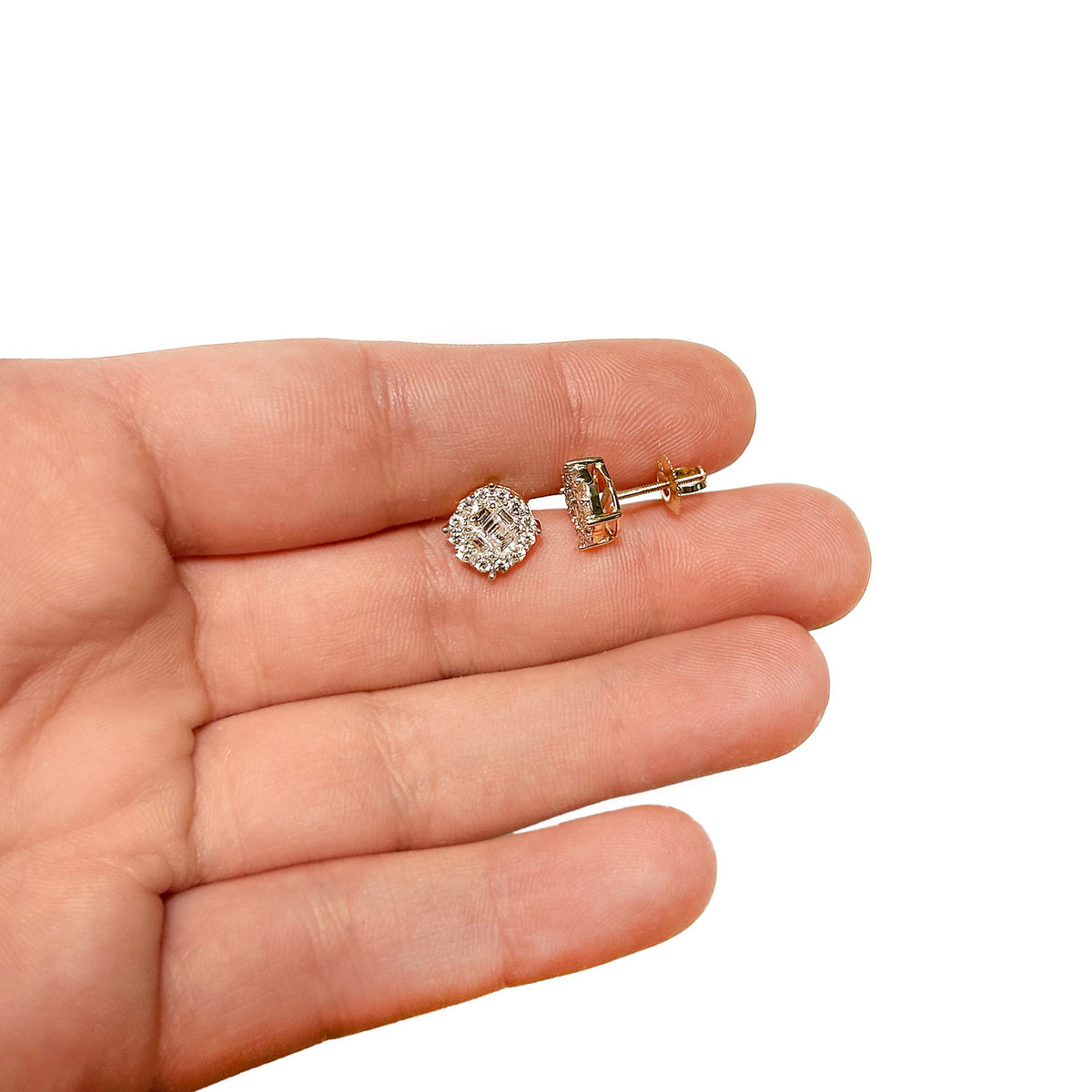 A pair of small gold stud earrings with clear gemstones, shown resting on an open hand against a plain white background. [lifestyle]