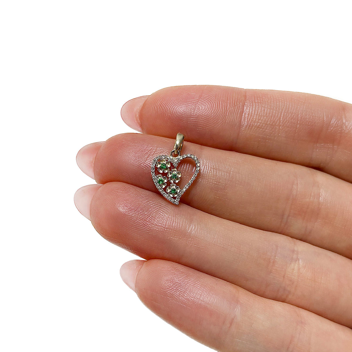 A small heart-shaped pendant with red and green stones, held between fingers to show its size against a plain white background. [lifestyle]
