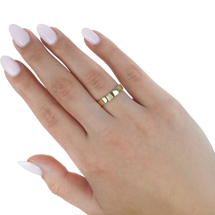 A close-up of a hand with pale pink manicured nails wearing a slim gold band ring with a small central clear gemstone, set against a plain white background. [lifestyle]