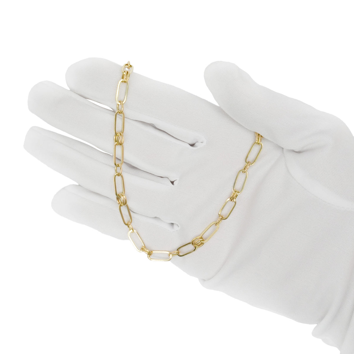 A gold paperclip chain necklace draped over a white-gloved hand against a plain white background. [lifestyle]