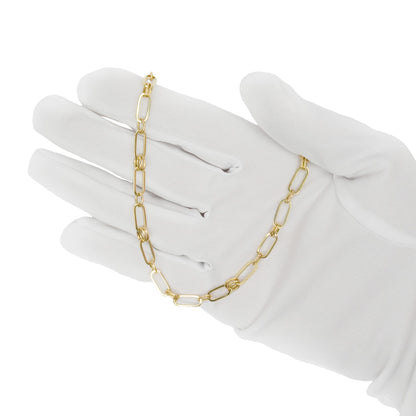 A gold paperclip chain necklace draped over a white-gloved hand against a plain white background. [lifestyle]