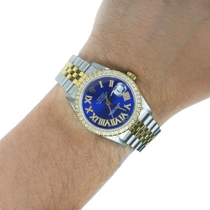 A two-tone Rolex Datejust watch with a blue dial, gold Roman numerals, and a diamond-encrusted bezel, shown worn on a person's wrist against a white background.[lifestyle]
