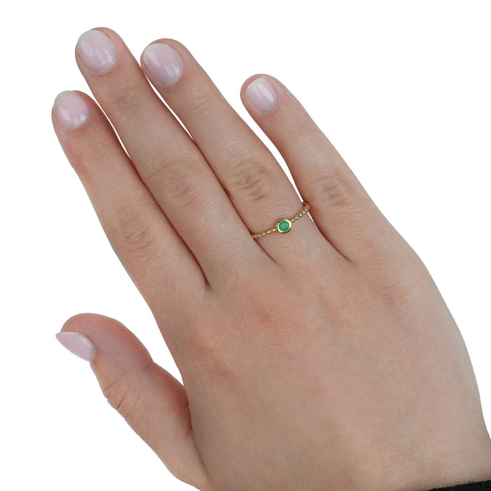 Hand wearing a gold ring with a green gemstone on a white background [lifestyle]