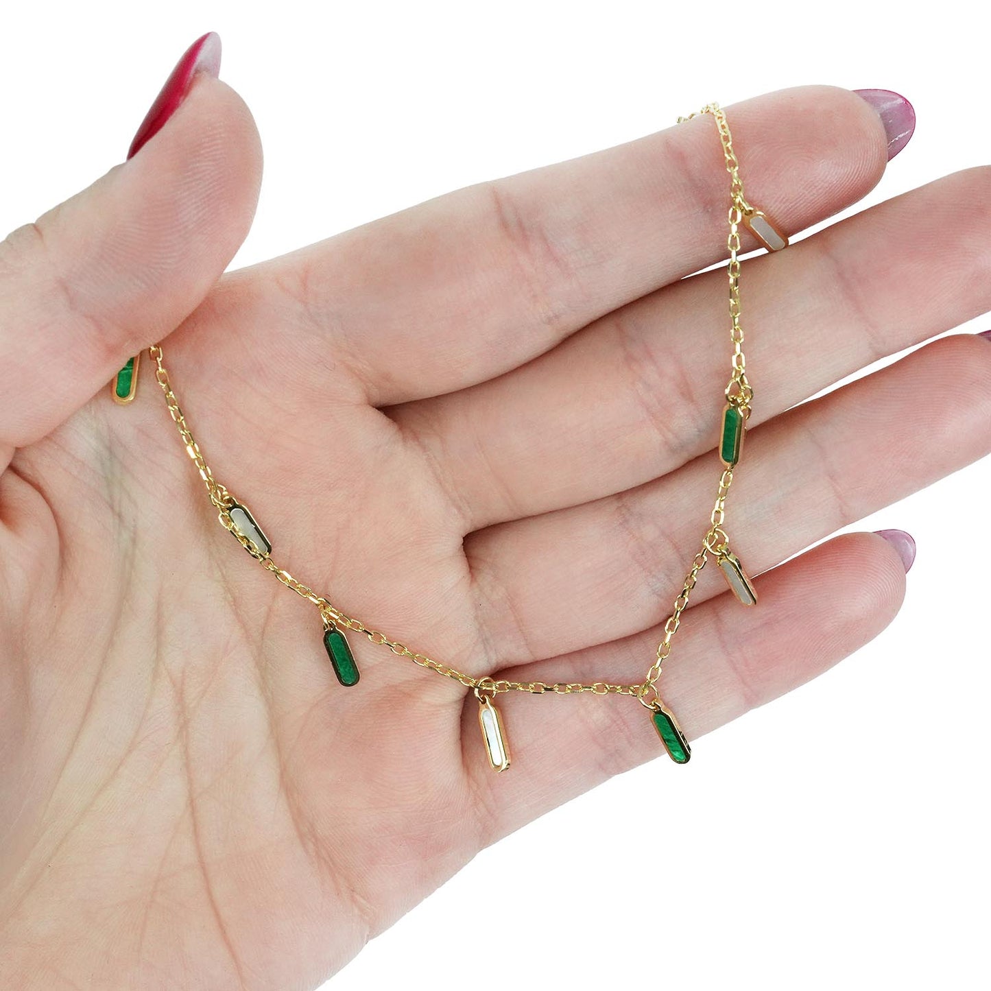 Gold chain necklace with green gemstones on a hand against a white background [lifestyle]