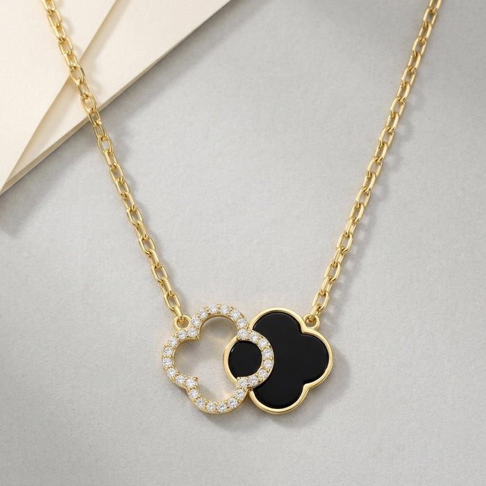 Gold necklace with black and white heart-shaped pendants on a gray surface [lifestyle]
