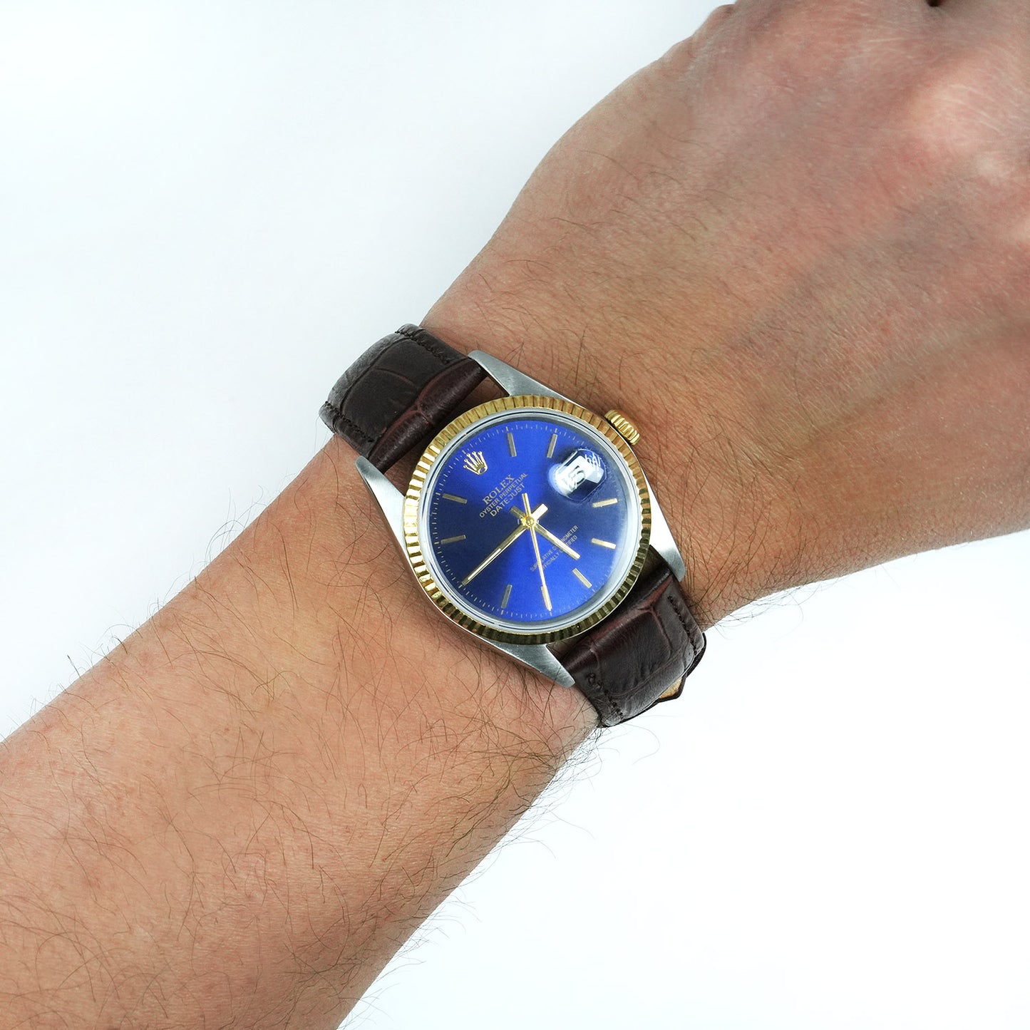 Wrist wearing a watch with a blue face and brown leather strap on a white background [lifestyle]