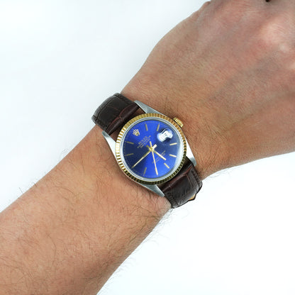 Wrist wearing a watch with a blue face and brown leather strap on a white background [lifestyle]
