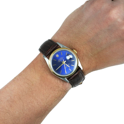 Wrist wearing a watch with a blue face and brown leather strap on a white background [lifestyle]