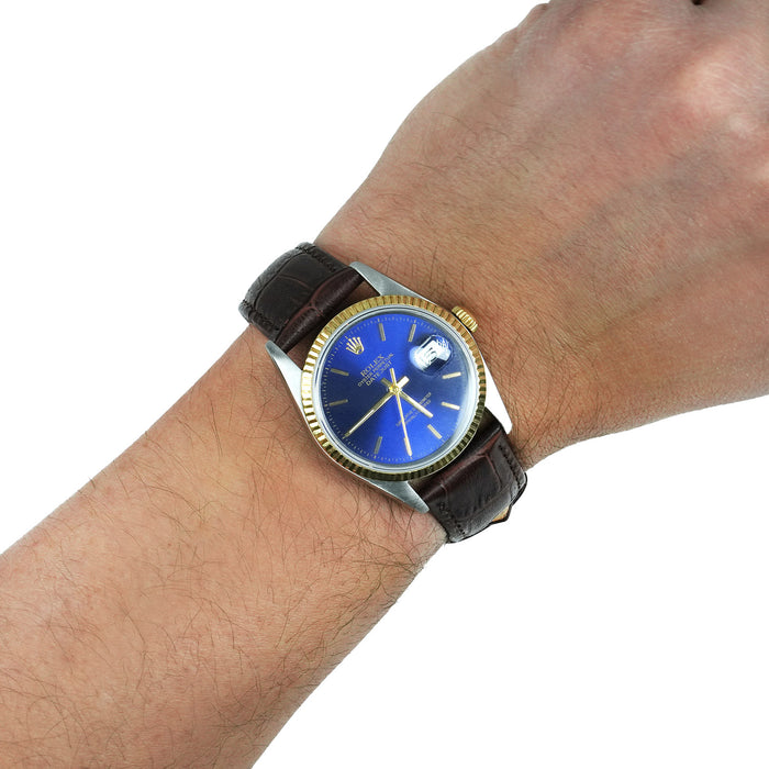 Wrist wearing a watch with a blue face and brown leather strap on a white background [lifestyle]