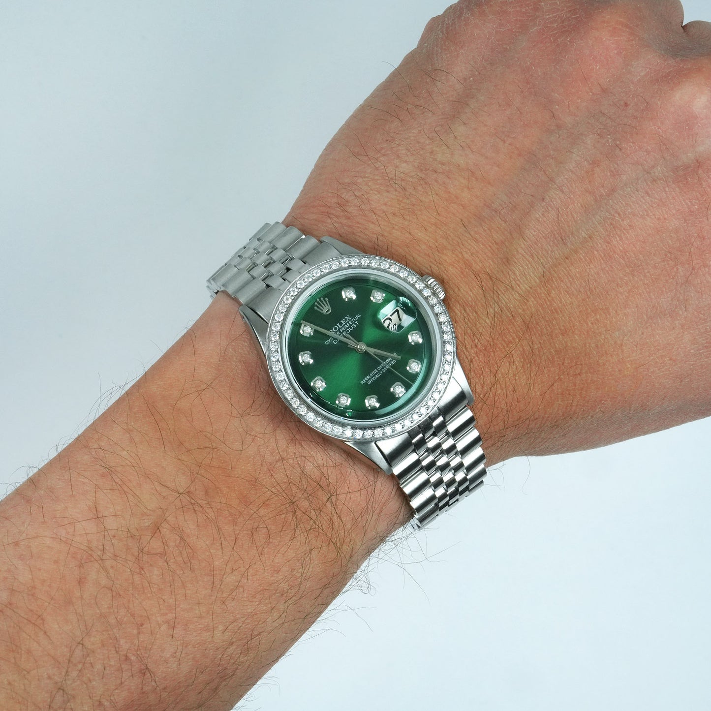 Green watch with silver bezel on a wrist against a light gray background [lifestyle]