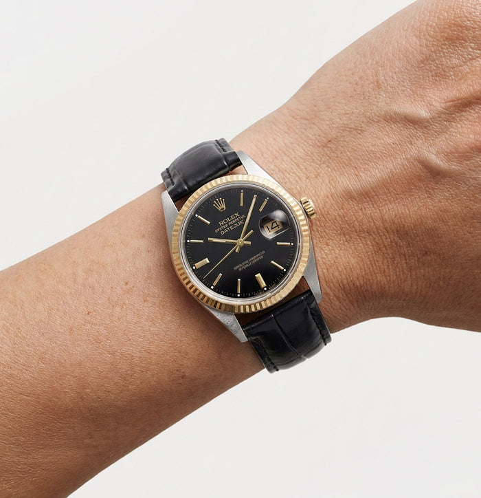 Luxury watch with black dial and gold accents on a wrist against a light gray background [lifestyle]