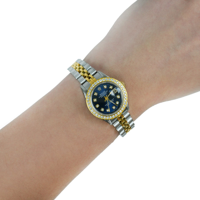 A two-tone stainless steel and yellow gold wristwatch with a blue dial and diamond bezel, shown worn on a person's wrist against a white background. [lifestyle]