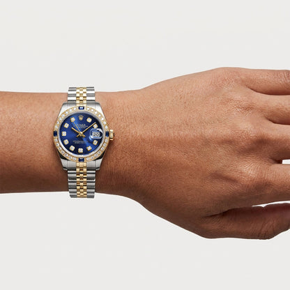 Hand wearing a two-tone watch with a blue face on a light gray background [lifestyle]