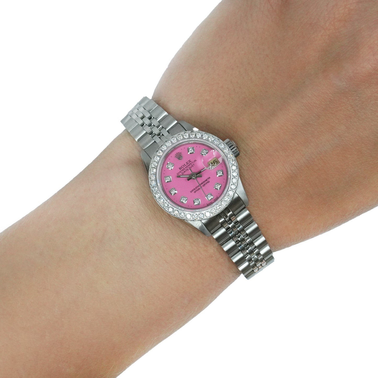 A silver-tone wristwatch with a pink mother-of-pearl dial and a diamond bezel, shown worn on a person's wrist against a white background. [lifestyle]