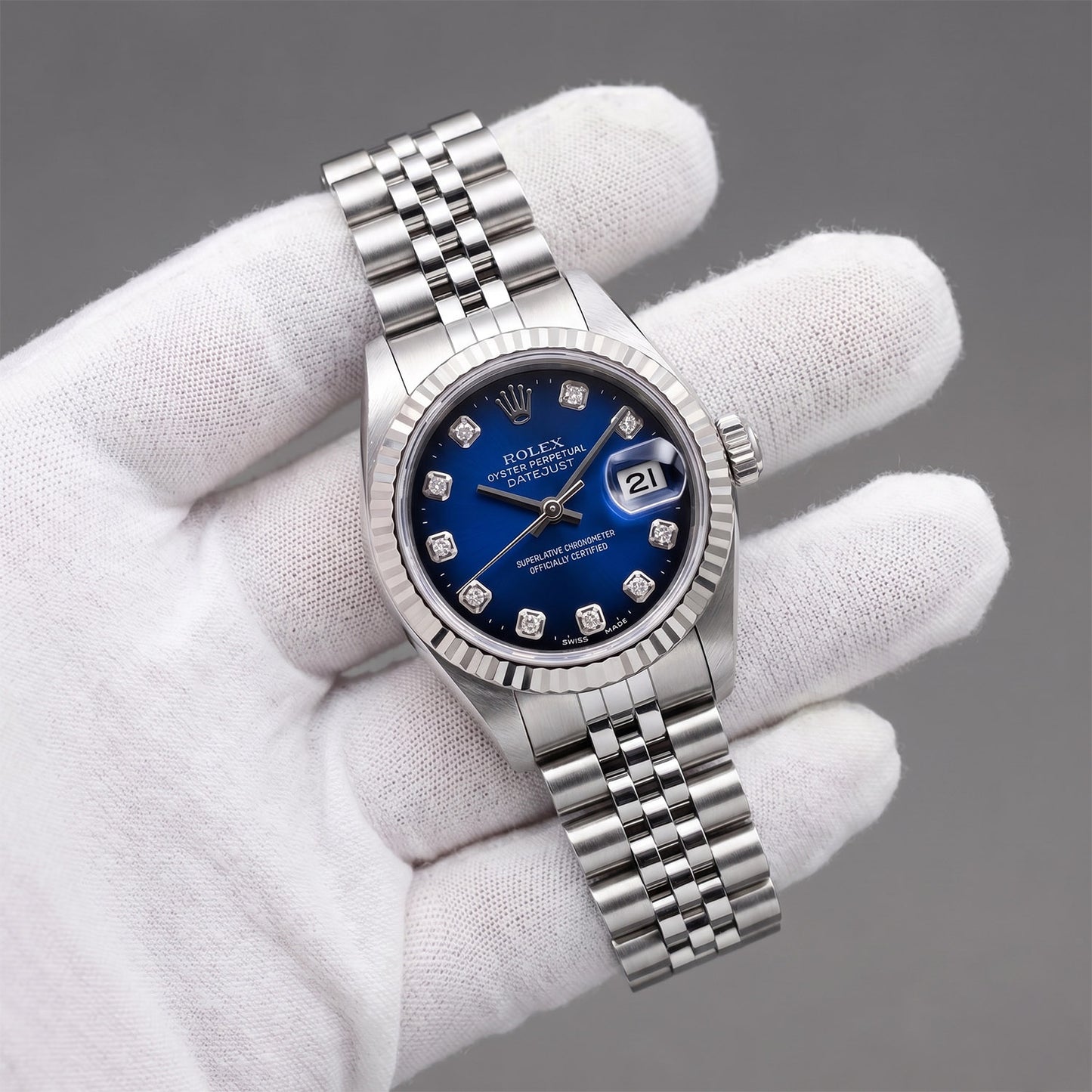 Silver watch with a blue face held by a gloved hand against a gray background [lifestyle]