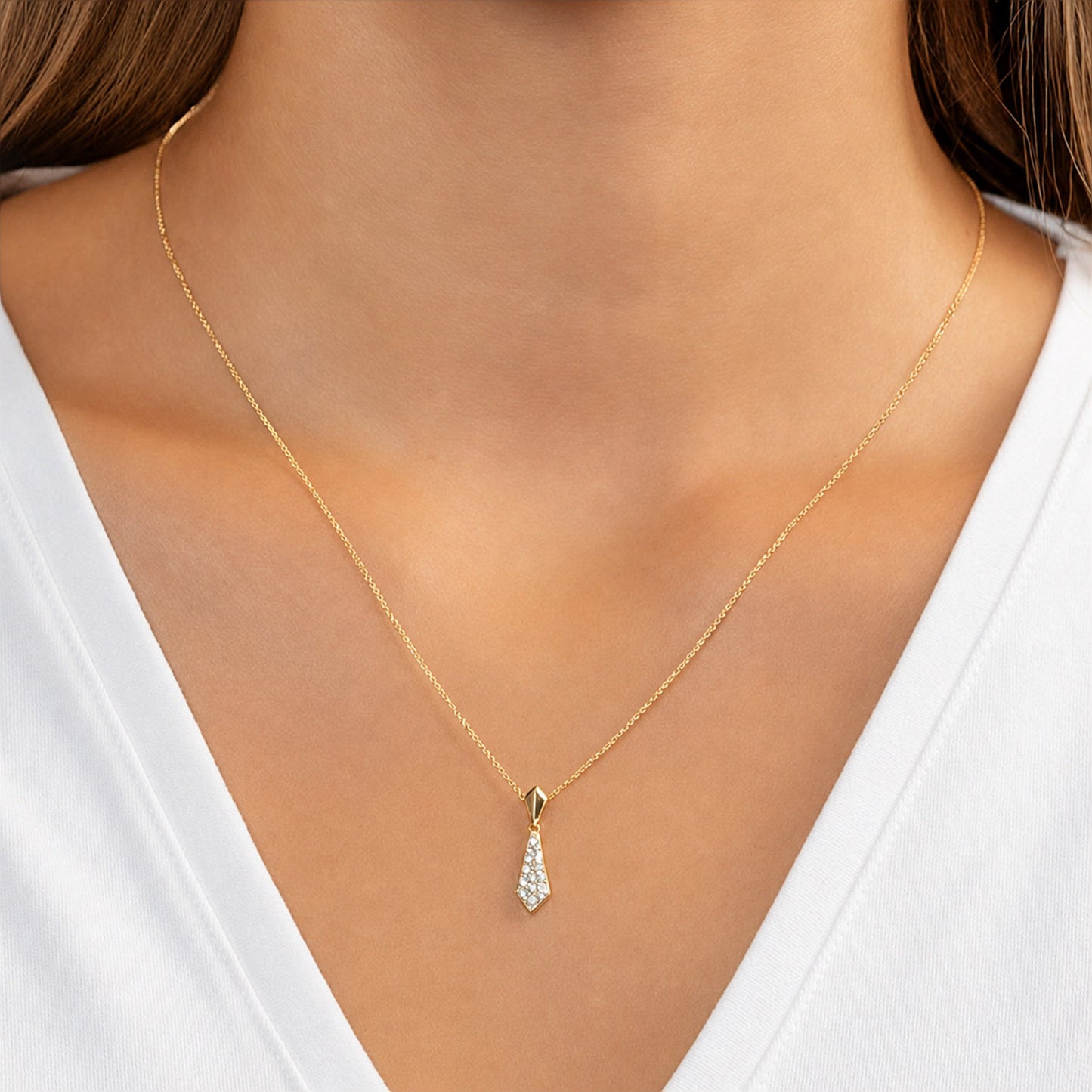 Gold necklace with a teardrop-shaped pendant on a person wearing a white top. [lifestyle]