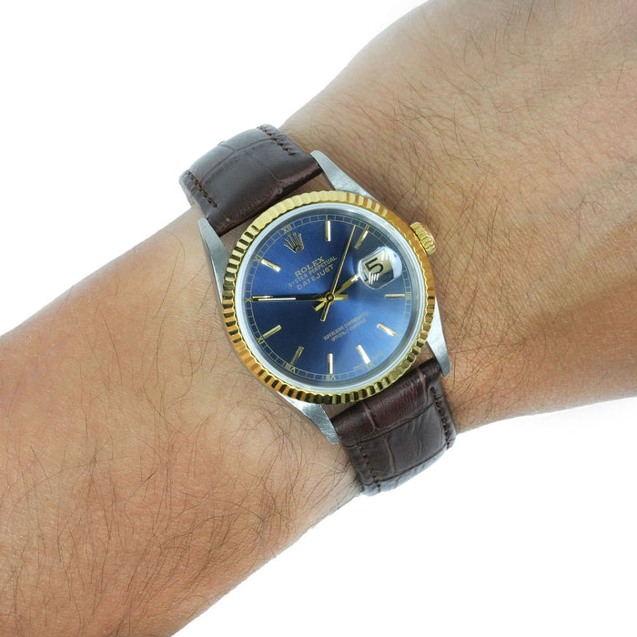A Rolex Datejust watch with a blue sunburst dial, gold-tone fluted bezel, and silver-tone case, shown worn on a person's wrist with a brown leather strap. [lifestyle]