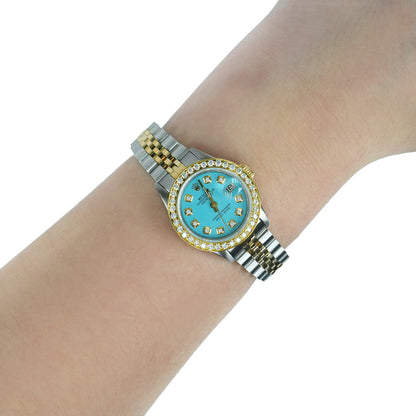 Gold and silver watch with a turquoise face on a wrist against a white background [lifestyle]