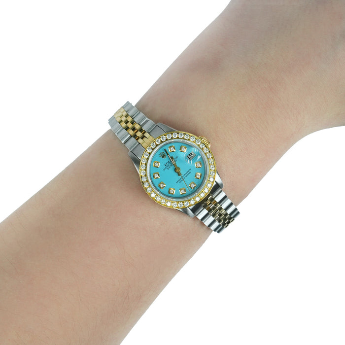 Gold and silver watch with a turquoise face on a wrist against a white background [lifestyle]