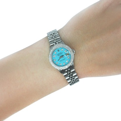 A Rolex Ladydate watch with a light blue dial, diamond hour markers, and a silver-tone Oyster bracelet, shown worn on a person's wrist against a white background. [lifestyle]