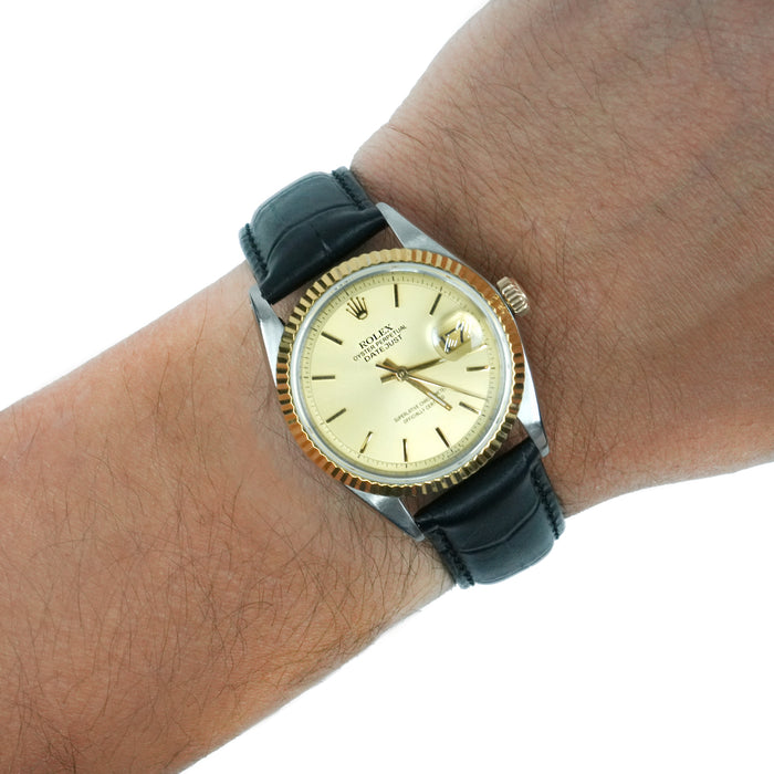 A Rolex Submariner watch with a gold dial, gold-tone fluted bezel, silver-tone case, and a black leather strap, shown worn on a person's wrist against a white background. [lifestyle]