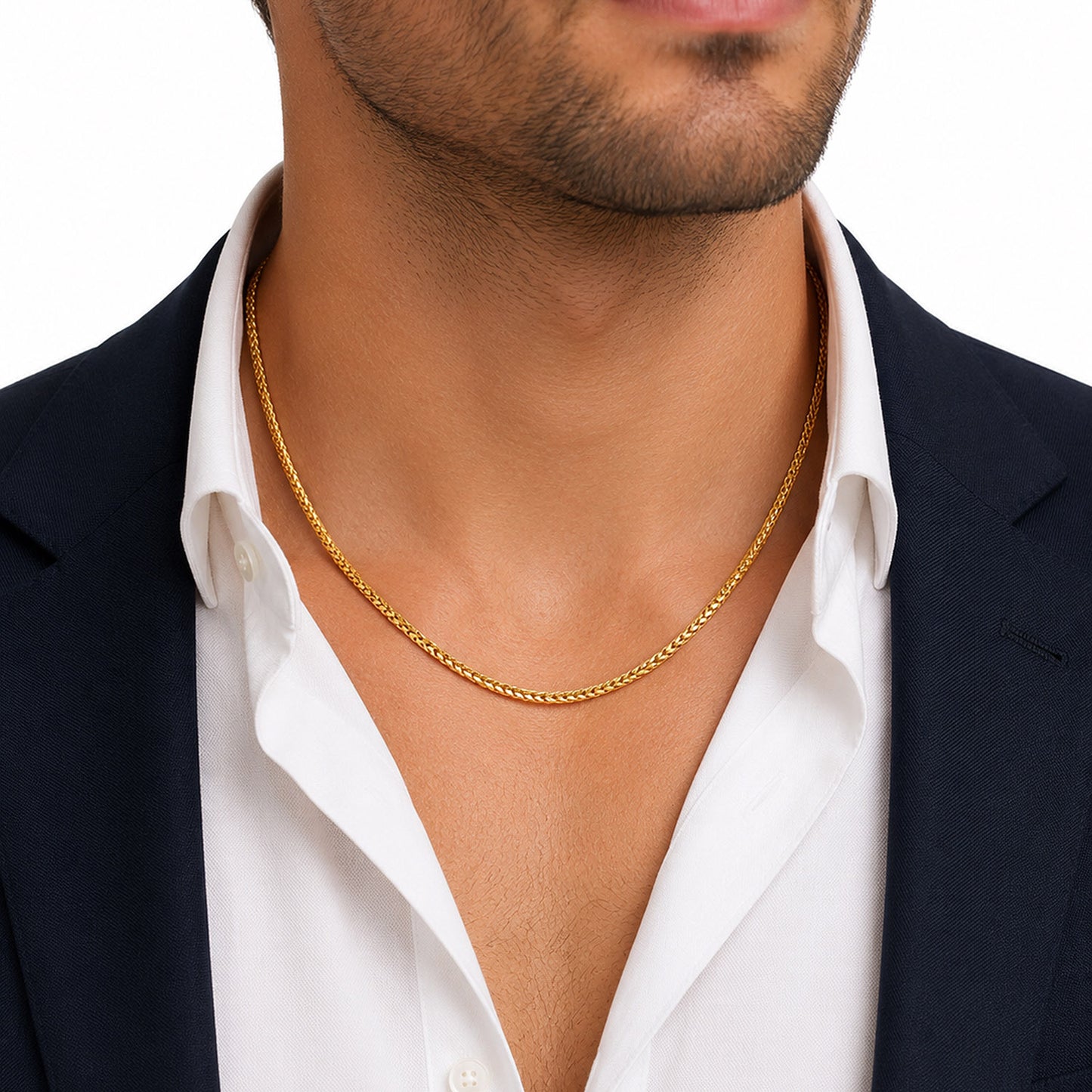 A close-up of a man wearing a delicate gold chain necklace over a white collared shirt and dark navy blazer, against a plain white background. [lifestyle]