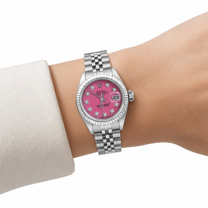 A Rolex Lady Day watch with a pink dial and diamond hour markers, worn on a wrist with a light-colored sleeve visible. [lifestyle]