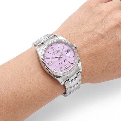 A Rolex Submariner Date watch with a silver stainless steel bracelet and fluted bezel, featuring a light pink dial, shown worn on a person's wrist against a white background. [lifestyle]