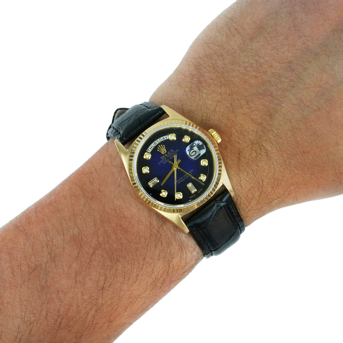A Rolex wristwatch with a gold case, black leather strap, and a dark blue dial with gold indices, shown worn on a person's wrist against a white background. [lifestyle]