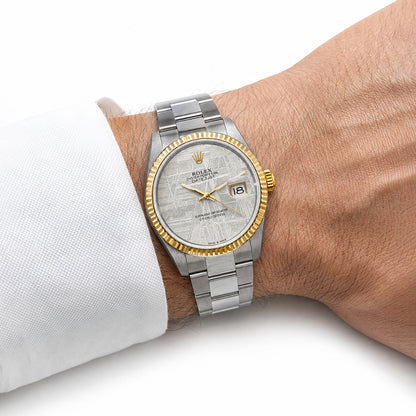 A Rolex Oyster Perpetual Datejust watch with a silver textured dial, gold-tone bezel, and two-tone stainless steel and yellow gold Oyster bracelet, shown on a person's wrist wearing a white dress shirt cuff. [lifestyle]