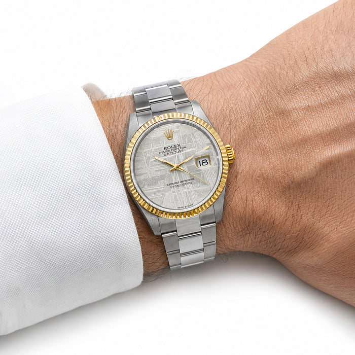 A Rolex Oyster Perpetual Datejust watch with a silver textured dial, gold-tone bezel, and two-tone stainless steel and yellow gold Oyster bracelet, shown on a person's wrist wearing a white dress shirt cuff. [lifestyle]