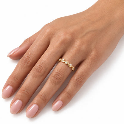 A close-up of a hand with light pink manicured nails wearing a delicate gold ring with small clear stones set in a wavy design, photographed against a clean white background. [lifestyle]