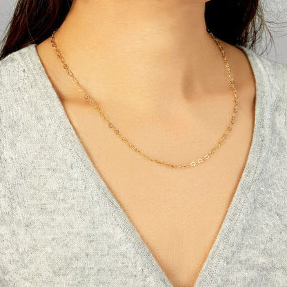 A delicate gold chain necklace worn by a model, shown in a close-up shot of the neck and chest wearing a gray V-neck top. [lifestyle]