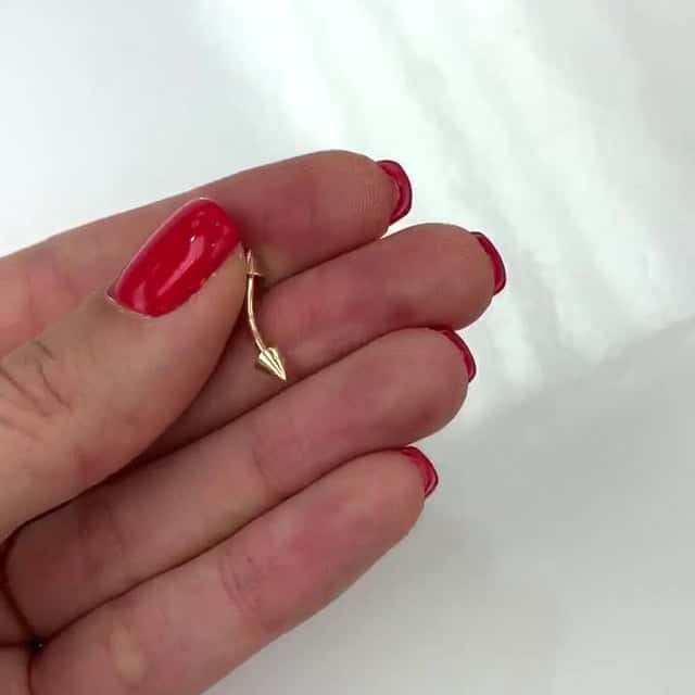 14k gold eyebrow spike barbell held between fingers with manicured red nails.