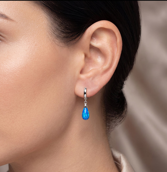 Close-up of a woman wearing an earring with a blue gemstone. [lifestyle]